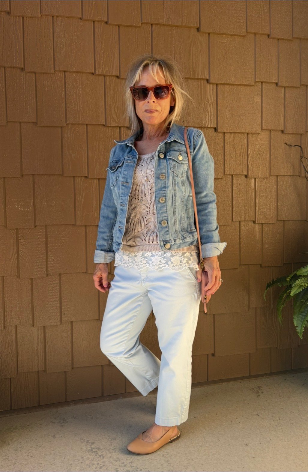 4'11" petite woman over 40 wearing a denim jacket with white ankle pants and flats
